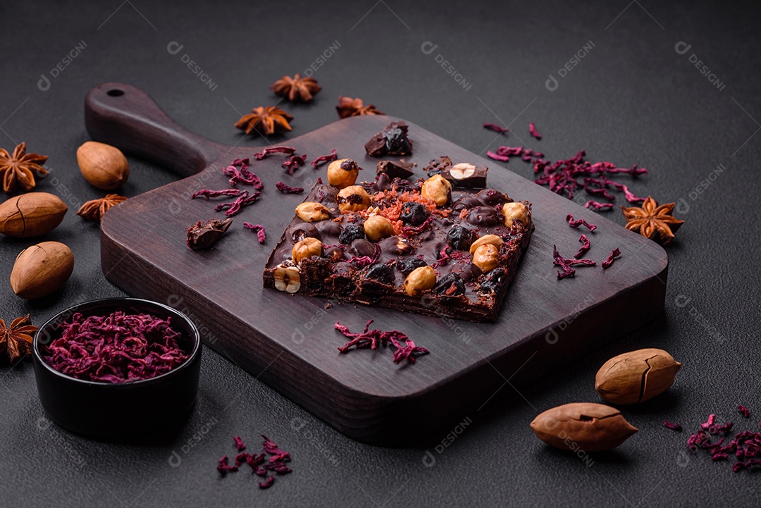 Chocolate artesanal com frutas, nozes e especiarias em um fundo escuro de concreto. Doces feitos em casa