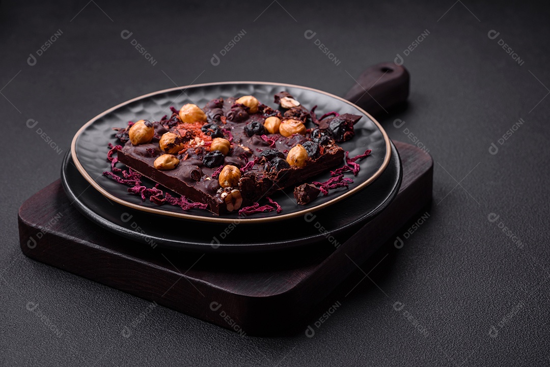 Chocolate artesanal com frutas, nozes e especiarias em um fundo escuro de concreto. Doces feitos em casa