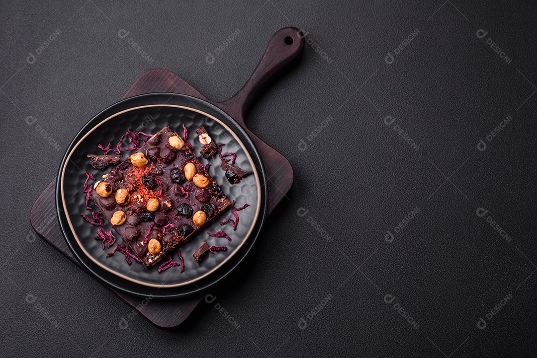 Chocolate artesanal com frutas, nozes e especiarias em um fundo escuro de concreto. Doces feitos em casa