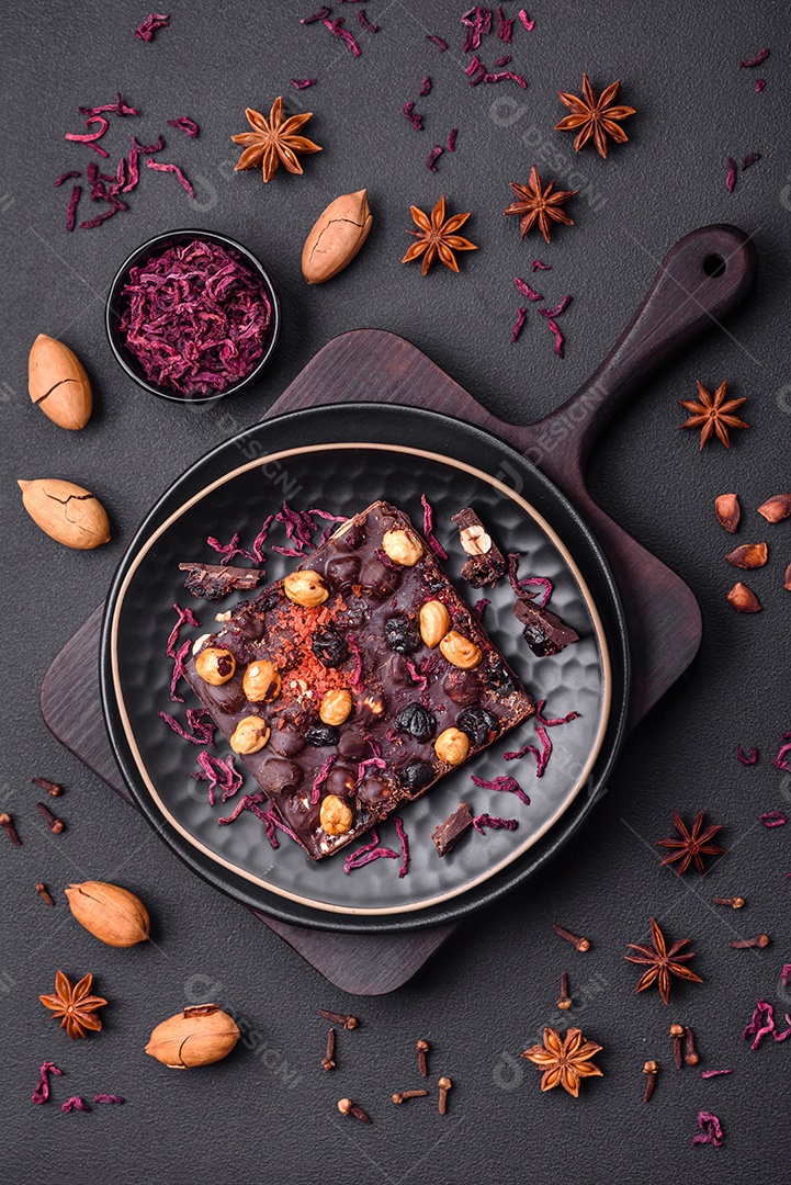 Chocolate artesanal com frutas, nozes e especiarias em um fundo escuro de concreto. Doces feitos em casa