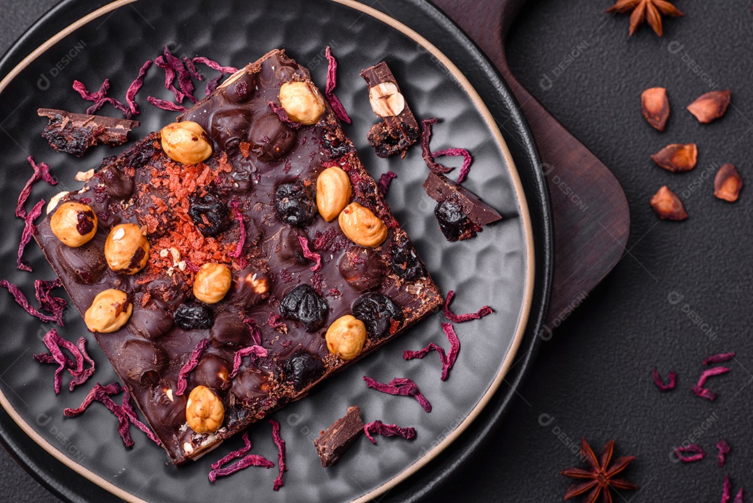 Chocolate artesanal com frutas, nozes e especiarias em um fundo escuro de concreto. Doces feitos em casa
