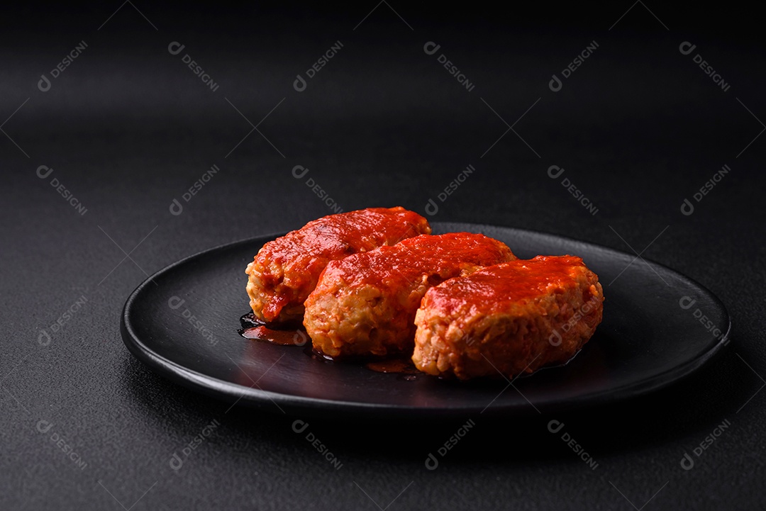 Costeleta de carne ou almôndegas em molho de tomate com alho, sal, especiarias e ervas em uma placa preta sobre um fundo escuro de concreto