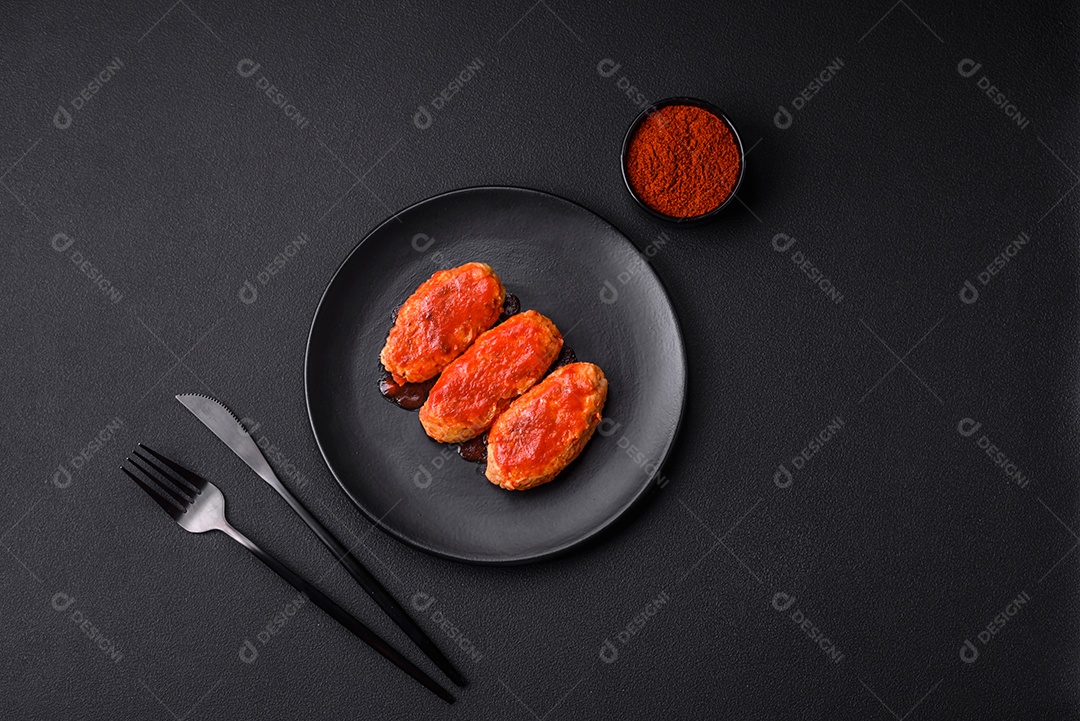 Costeleta de carne ou almôndegas em molho de tomate com alho, sal, especiarias e ervas em uma placa preta sobre um fundo escuro de concreto