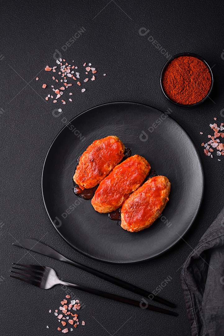 Costeleta de carne ou almôndegas em molho de tomate com alho, sal, especiarias e ervas em uma placa preta sobre um fundo escuro de concreto