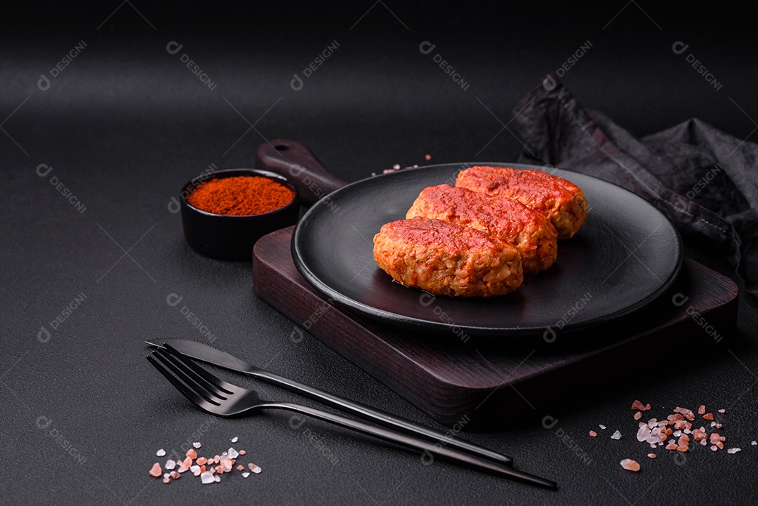 Costeleta de carne ou almôndegas em molho de tomate com alho, sal, especiarias e ervas em uma placa preta sobre um fundo escuro de concreto