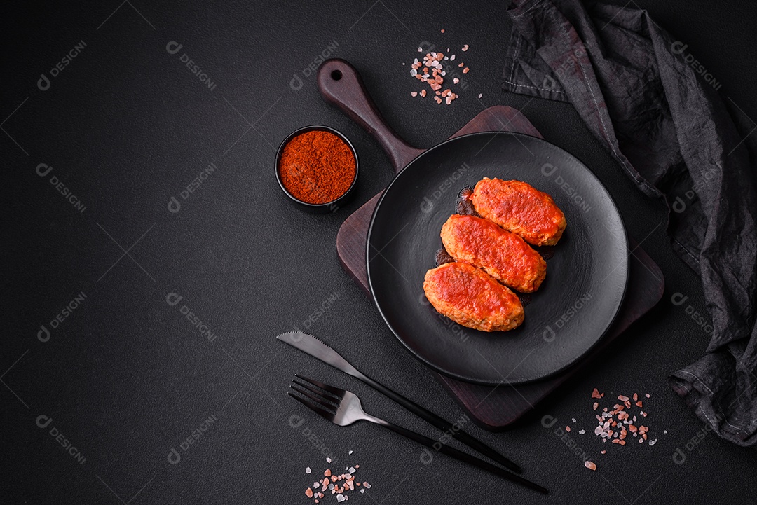 Costeleta de carne ou almôndegas em molho de tomate com alho, sal, especiarias e ervas em uma placa preta sobre um fundo escuro de concreto