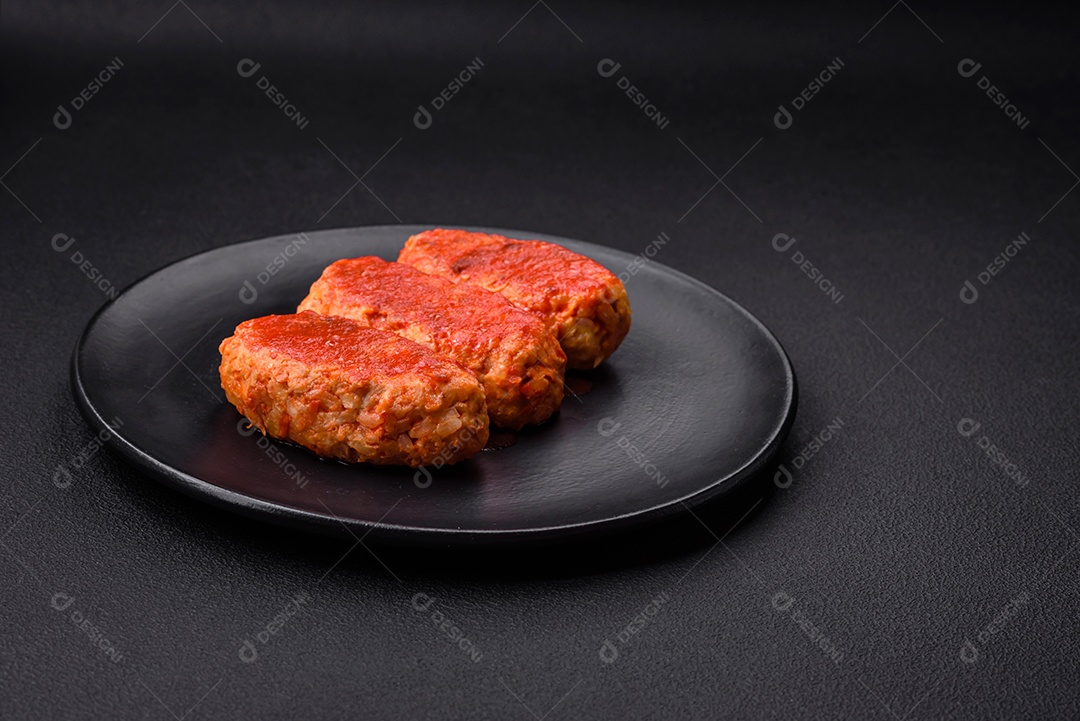 Costeleta de carne ou almôndegas em molho de tomate com alho, sal, especiarias e ervas em uma placa preta sobre um fundo escuro de concreto