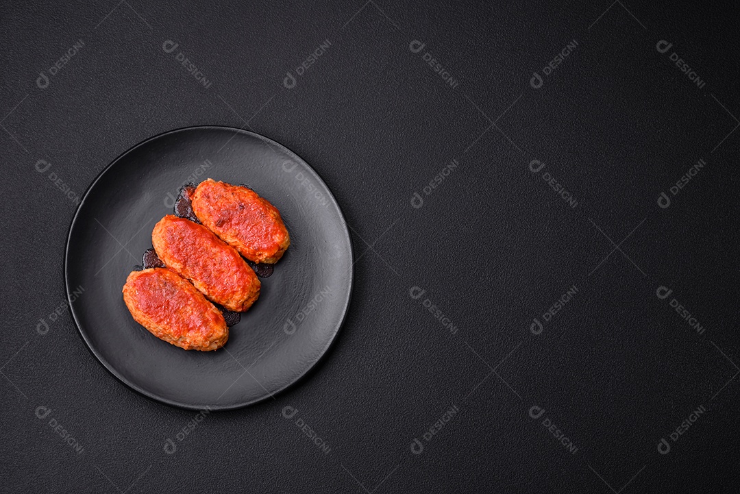 Costeleta de carne ou almôndegas em molho de tomate com alho, sal, especiarias e ervas em uma placa preta sobre um fundo escuro de concreto