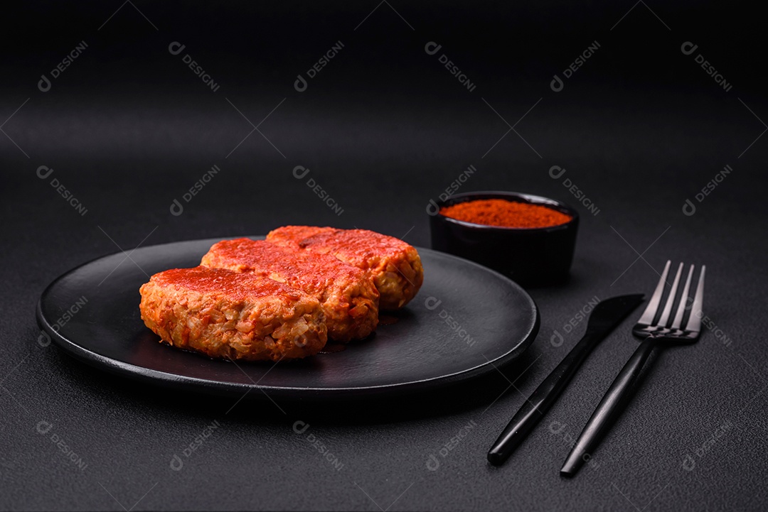 Costeleta de carne ou almôndegas em molho de tomate com alho, sal, especiarias e ervas em uma placa preta sobre um fundo escuro de concreto