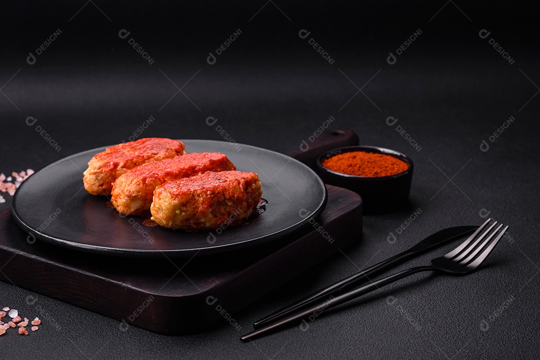 Costeleta de carne ou almôndegas em molho de tomate com alho, sal, especiarias e ervas em uma placa preta sobre um fundo escuro de concreto