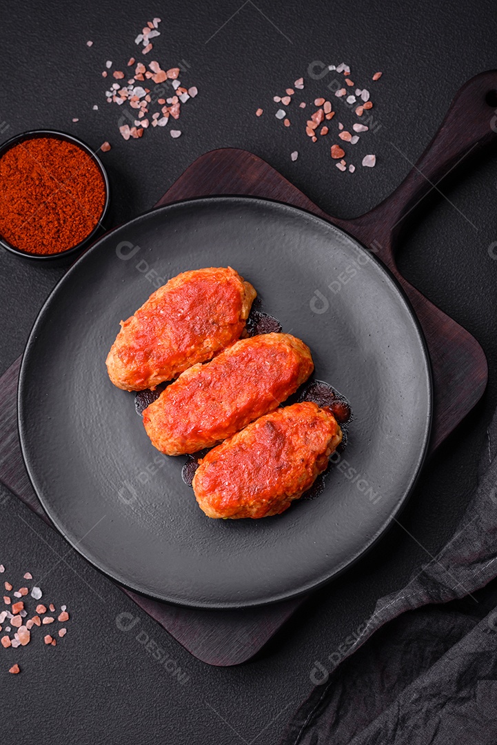 Costeleta de carne ou almôndegas em molho de tomate com alho, sal, especiarias e ervas em uma placa preta sobre um fundo escuro de concreto