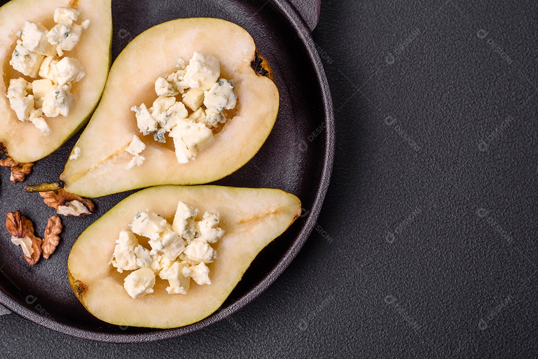 Deliciosa pêra assada com queijo dorblu, nozes e mel sobre um fundo de concreto texturizado. Prato vegetariano