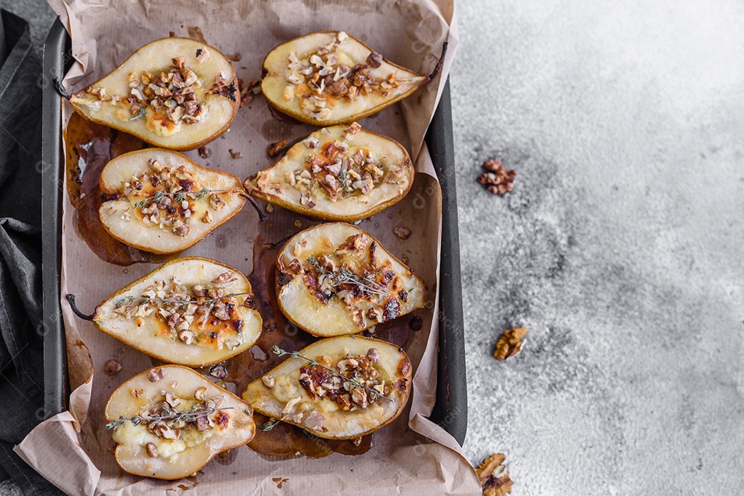 Deliciosa pêra assada com queijo dorblu, nozes e mel sobre um fundo de concreto texturizado. Prato vegetariano
