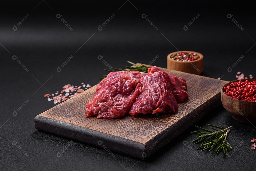 Carne crua cortada em vários pedaços sobre uma tábua de madeira sobre um fundo escuro de concreto