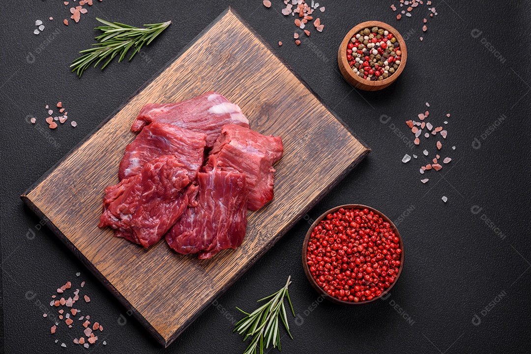 Carne crua cortada em vários pedaços sobre uma tábua de madeira sobre um fundo escuro de concreto