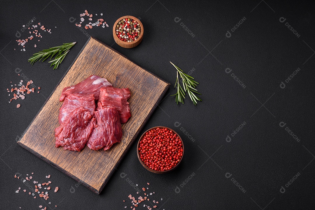 Carne crua cortada em vários pedaços sobre uma tábua de madeira sobre um fundo escuro de concreto