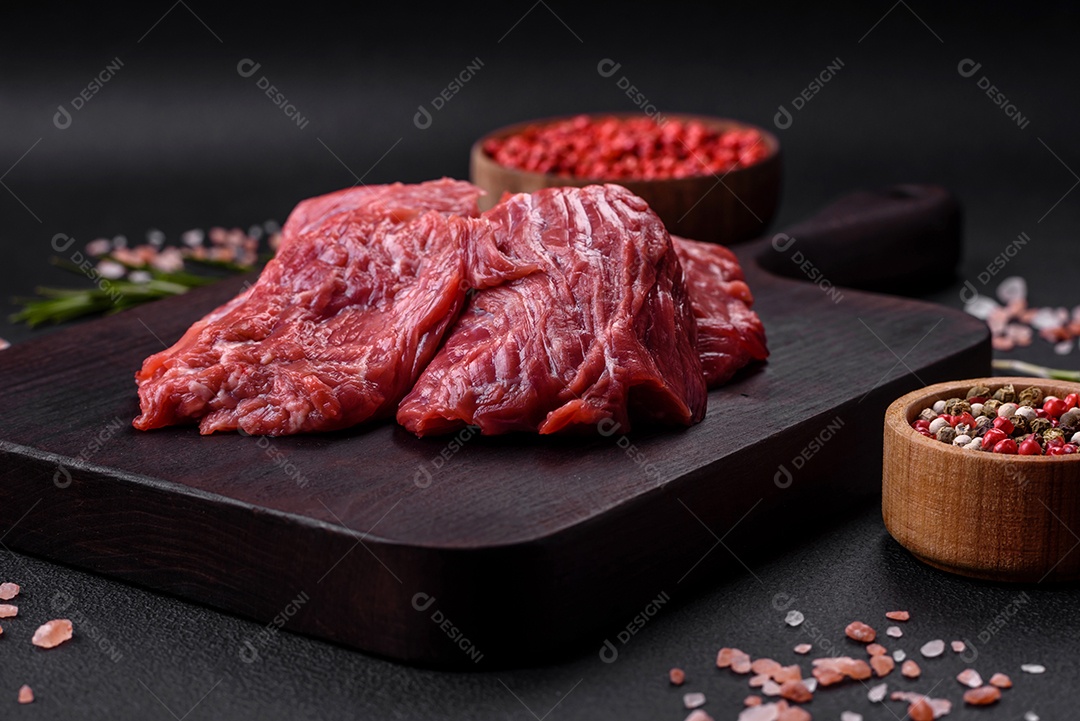 Carne crua cortada em vários pedaços sobre uma tábua de madeira sobre um fundo escuro de concreto
