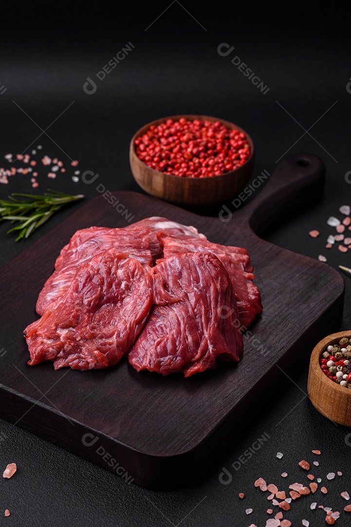 Carne crua cortada em vários pedaços sobre uma tábua de madeira sobre um fundo escuro de concreto
