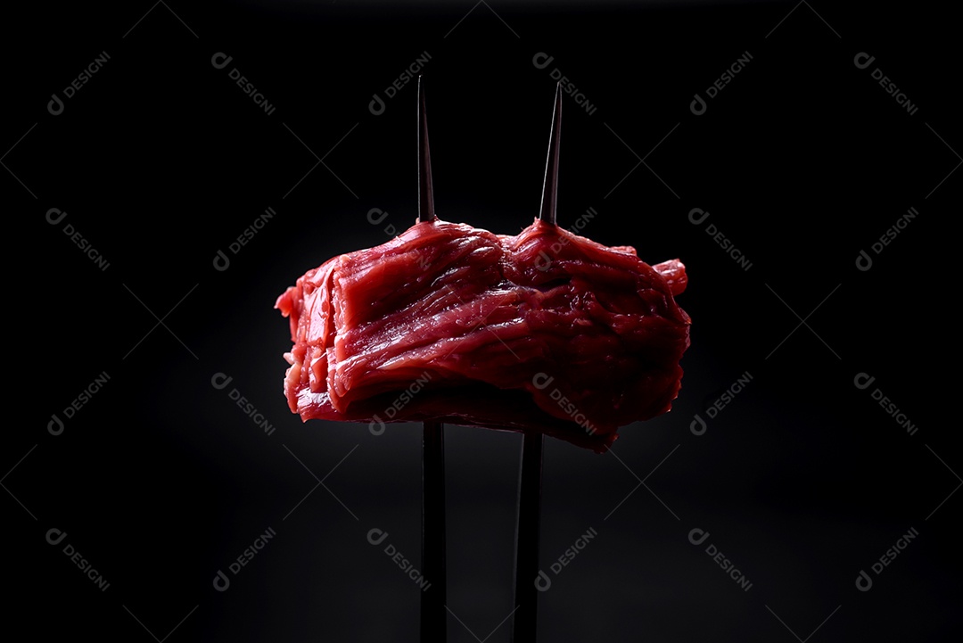 Carne crua cortada em vários pedaços sobre uma tábua de madeira sobre um fundo escuro de concreto