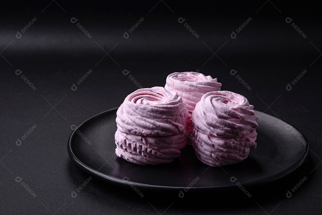 Deliciosos marshmallows arejados naturais e frescos em uma placa de cerâmica preta sobre um fundo escuro de concreto