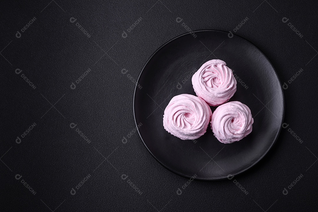 Deliciosos marshmallows arejados naturais e frescos em uma placa de cerâmica preta sobre um fundo escuro de concreto