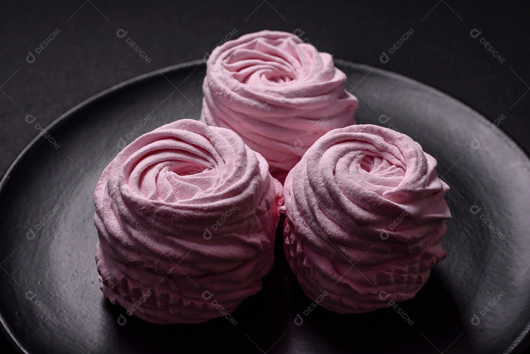 Deliciosos marshmallows arejados naturais e frescos em uma placa de cerâmica preta sobre um fundo escuro de concreto