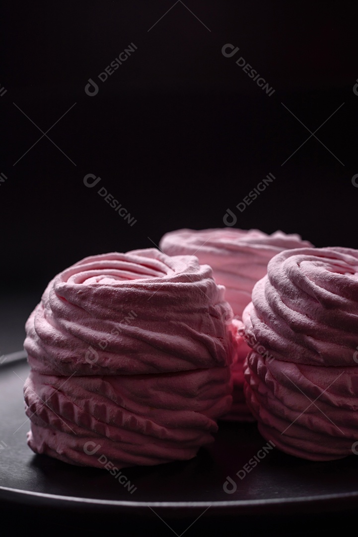 Deliciosos marshmallows arejados naturais e frescos em uma placa de cerâmica preta sobre um fundo escuro de concreto