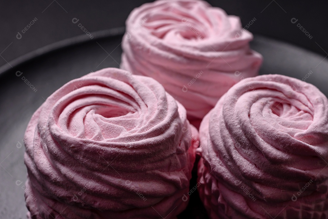 Deliciosos marshmallows arejados naturais e frescos em uma placa de cerâmica preta sobre um fundo escuro de concreto