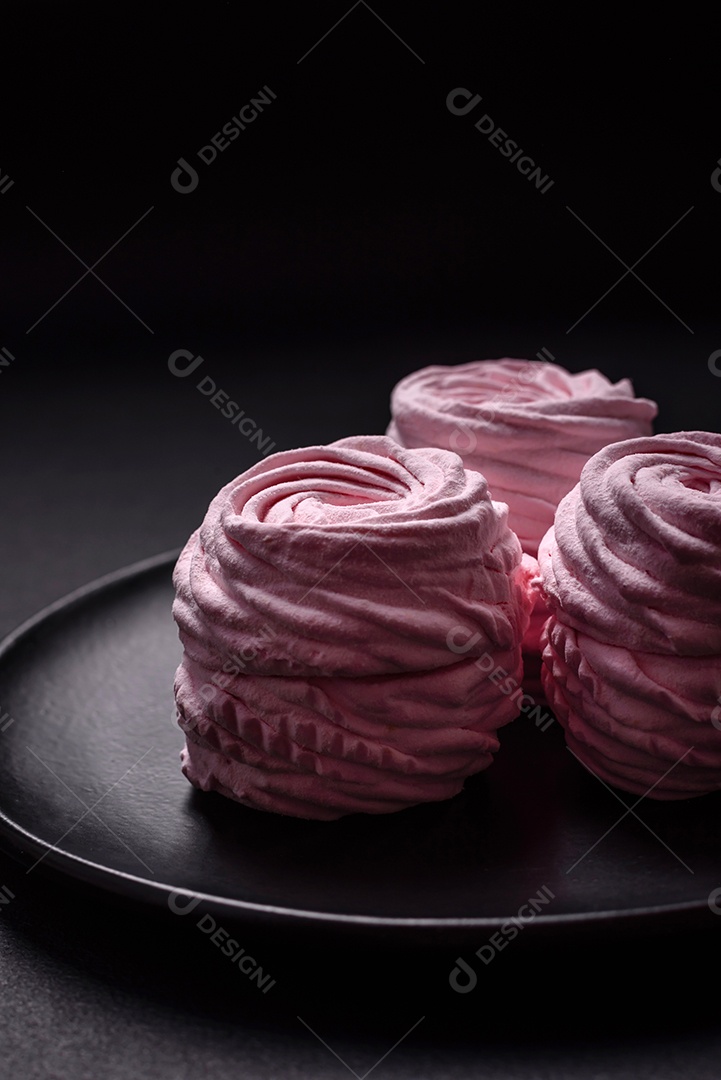 Deliciosos marshmallows arejados naturais e frescos em uma placa de cerâmica preta sobre um fundo escuro de concreto