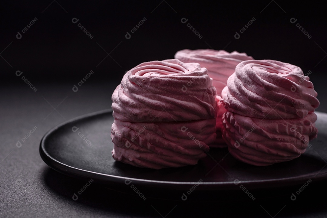 Deliciosos marshmallows arejados naturais e frescos em uma placa de cerâmica preta sobre um fundo escuro de concreto