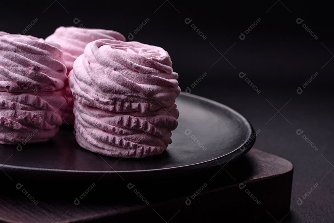 Deliciosos marshmallows arejados naturais e frescos em uma placa de cerâmica preta sobre um fundo escuro de concreto