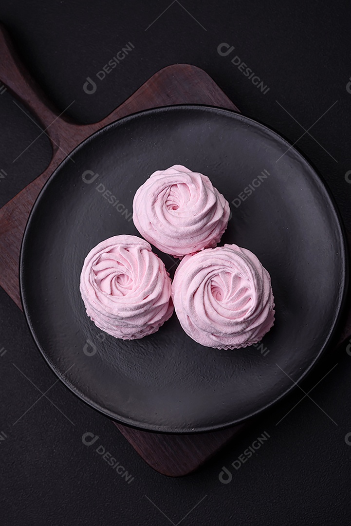 Deliciosos marshmallows arejados naturais e frescos em uma placa de cerâmica preta sobre um fundo escuro de concreto