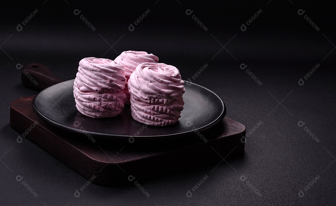 Deliciosos marshmallows arejados naturais e frescos em uma placa de cerâmica preta sobre um fundo escuro de concreto