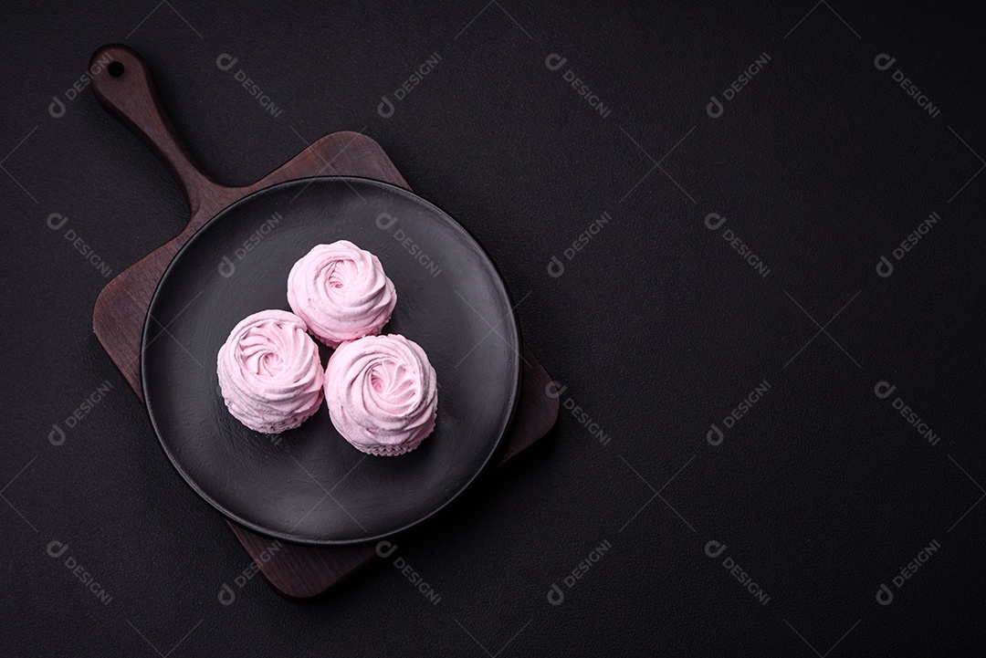 Deliciosos marshmallows arejados naturais e frescos em uma placa de cerâmica preta sobre um fundo escuro de concreto