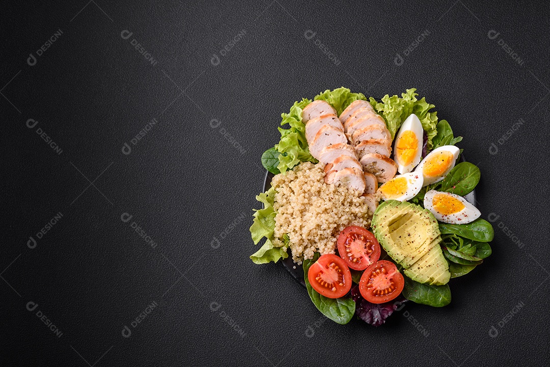 Delicioso almoço saudável composto por frango, abacate, quinoa, ovos, tomate, alface e verduras em uma placa preta sobre fundo de concreto