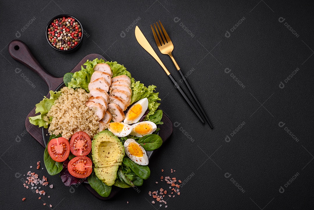 Delicioso almoço saudável composto por frango, abacate, quinoa, ovos, tomate, alface e verduras em uma placa preta sobre fundo de concreto