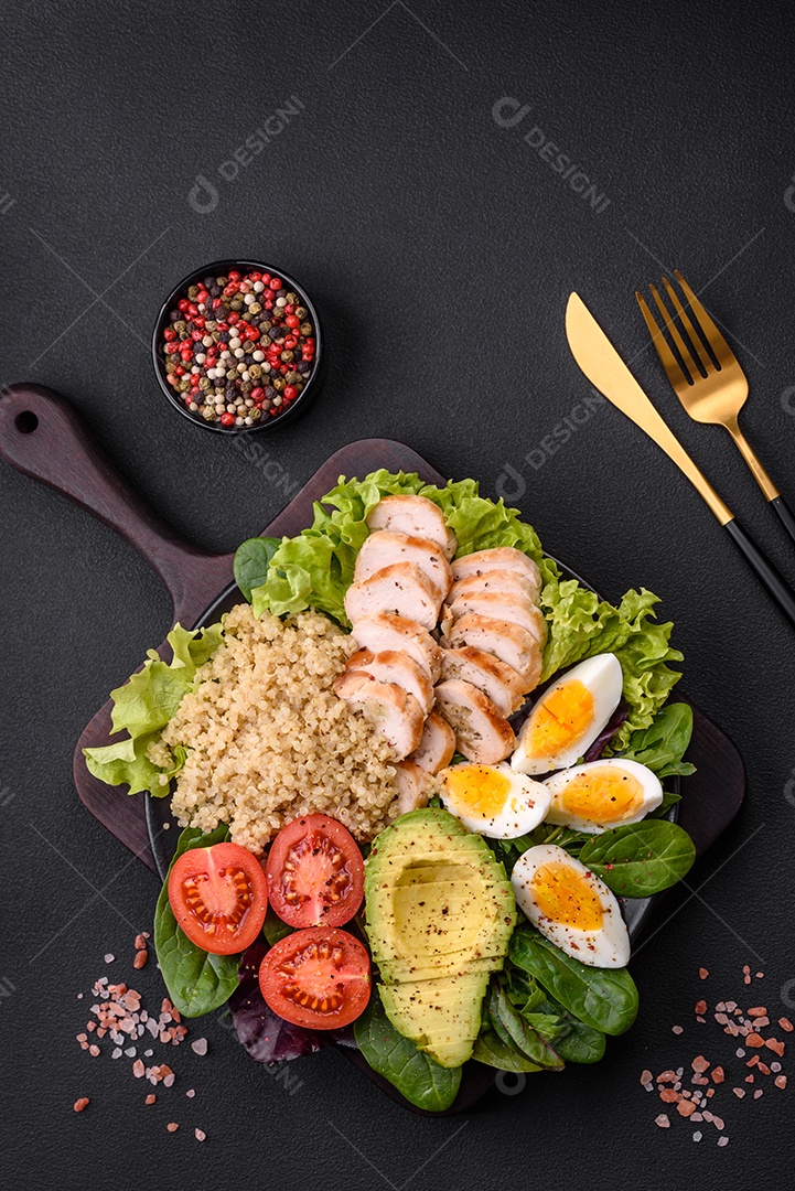 Delicioso almoço saudável composto por frango, abacate, quinoa, ovos, tomate, alface e verduras em uma placa preta sobre fundo de concreto
