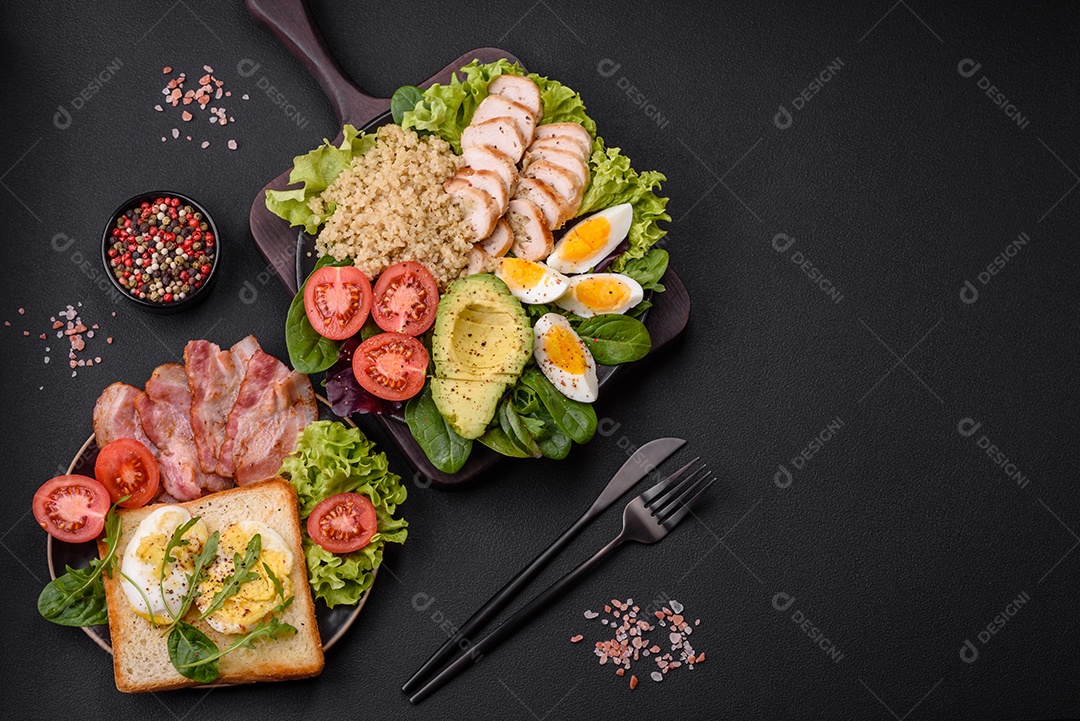 Delicioso almoço saudável composto por frango, abacate, quinoa, ovos, tomate, alface e verduras em uma placa preta sobre fundo de concreto