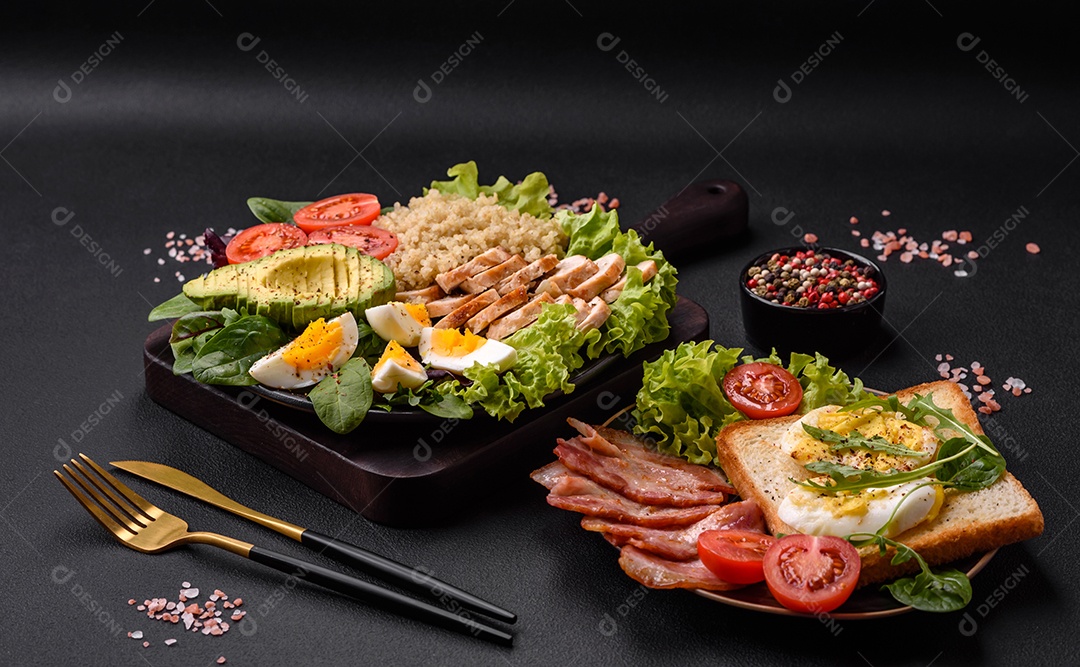 Delicioso almoço saudável composto por frango, abacate, quinoa, ovos, tomate, alface e verduras em uma placa preta sobre fundo de concreto