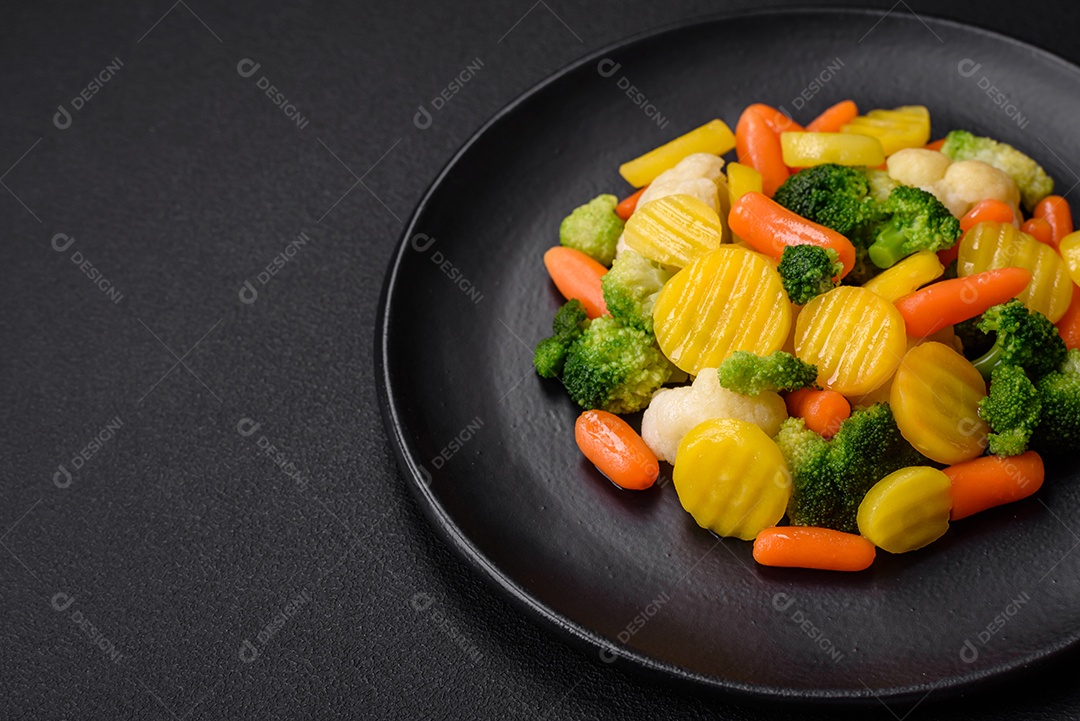 Deliciosos legumes frescos cozidos cenouras, brócolis, couve-flor em uma placa preta sobre um fundo escuro de concreto