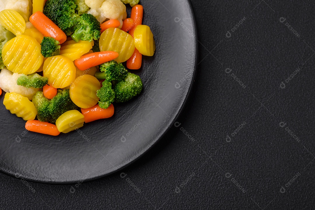 Deliciosos legumes frescos cozidos cenouras, brócolis, couve-flor em uma placa preta sobre um fundo escuro de concreto