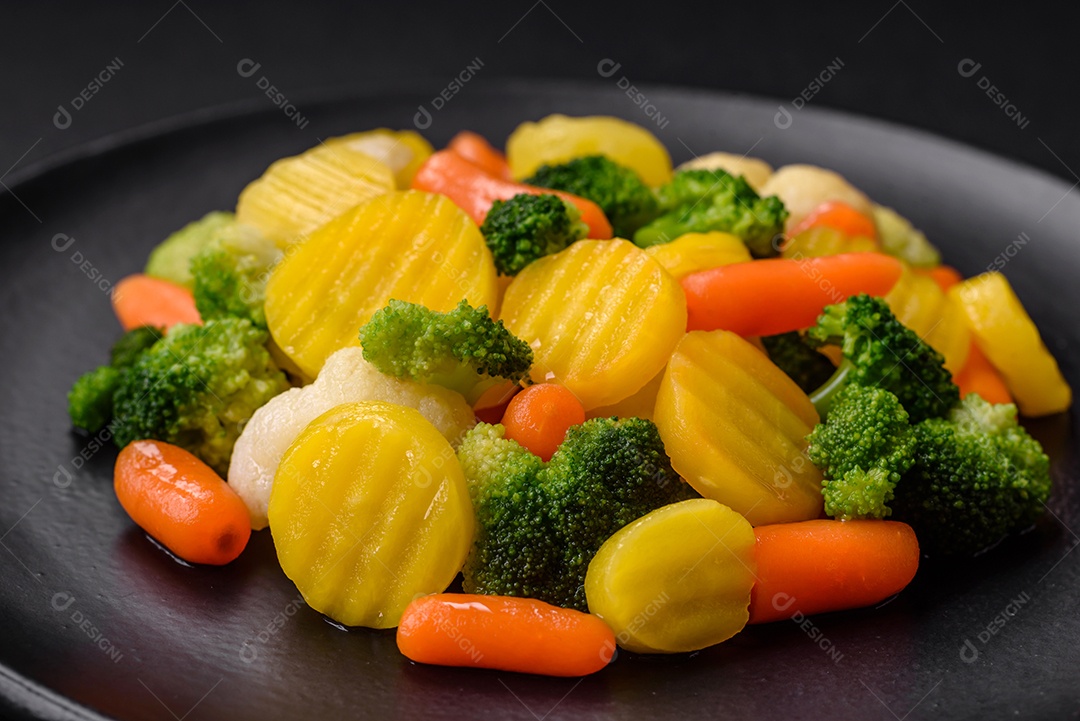 Deliciosos legumes frescos cozidos cenouras, brócolis, couve-flor em uma placa preta sobre um fundo escuro de concreto