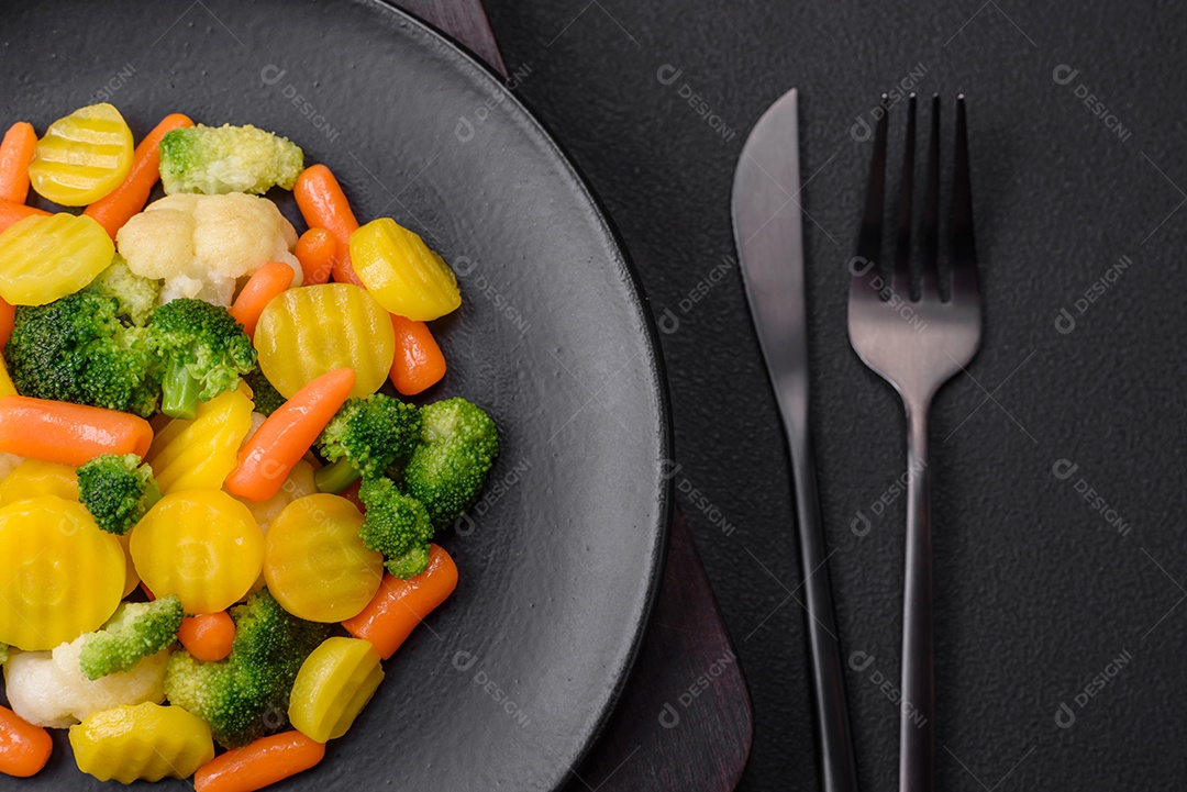 Deliciosos legumes frescos cozidos cenouras, brócolis, couve-flor em uma placa preta sobre um fundo escuro de concreto