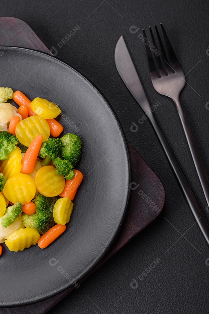 Deliciosos legumes frescos cozidos cenouras, brócolis, couve-flor em uma placa preta sobre um fundo escuro de concreto