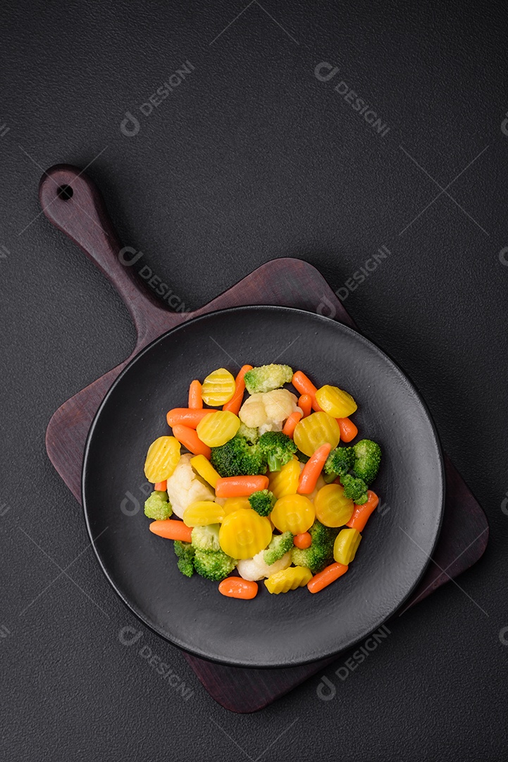 Deliciosos legumes frescos cozidos cenouras, brócolis, couve-flor em uma placa preta sobre um fundo escuro de concreto