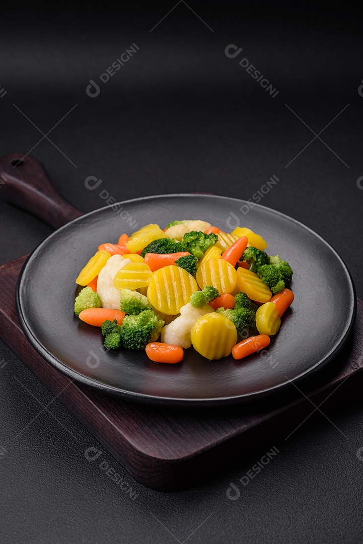 Deliciosos legumes frescos cozidos cenouras, brócolis, couve-flor em uma placa preta sobre um fundo escuro de concreto