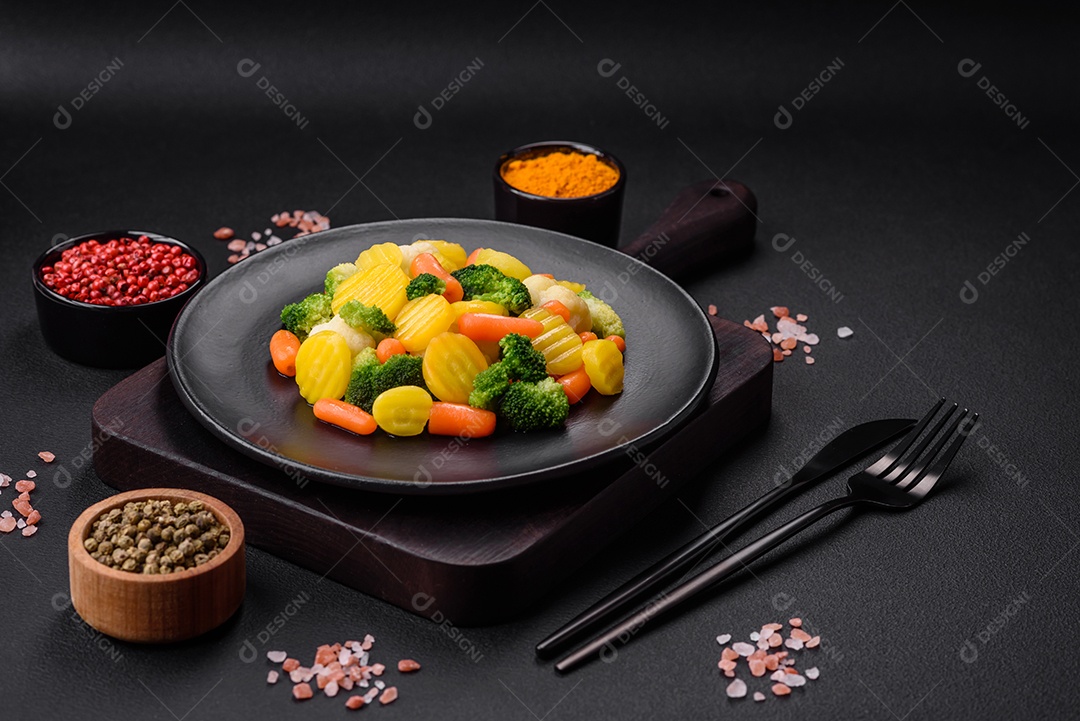 Deliciosos legumes frescos cozidos cenouras, brócolis, couve-flor em uma placa preta sobre um fundo escuro de concreto