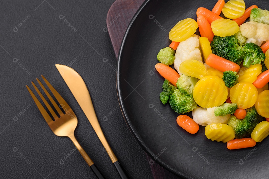 Deliciosos legumes frescos cozidos cenouras, brócolis, couve-flor em uma placa preta sobre um fundo escuro de concreto