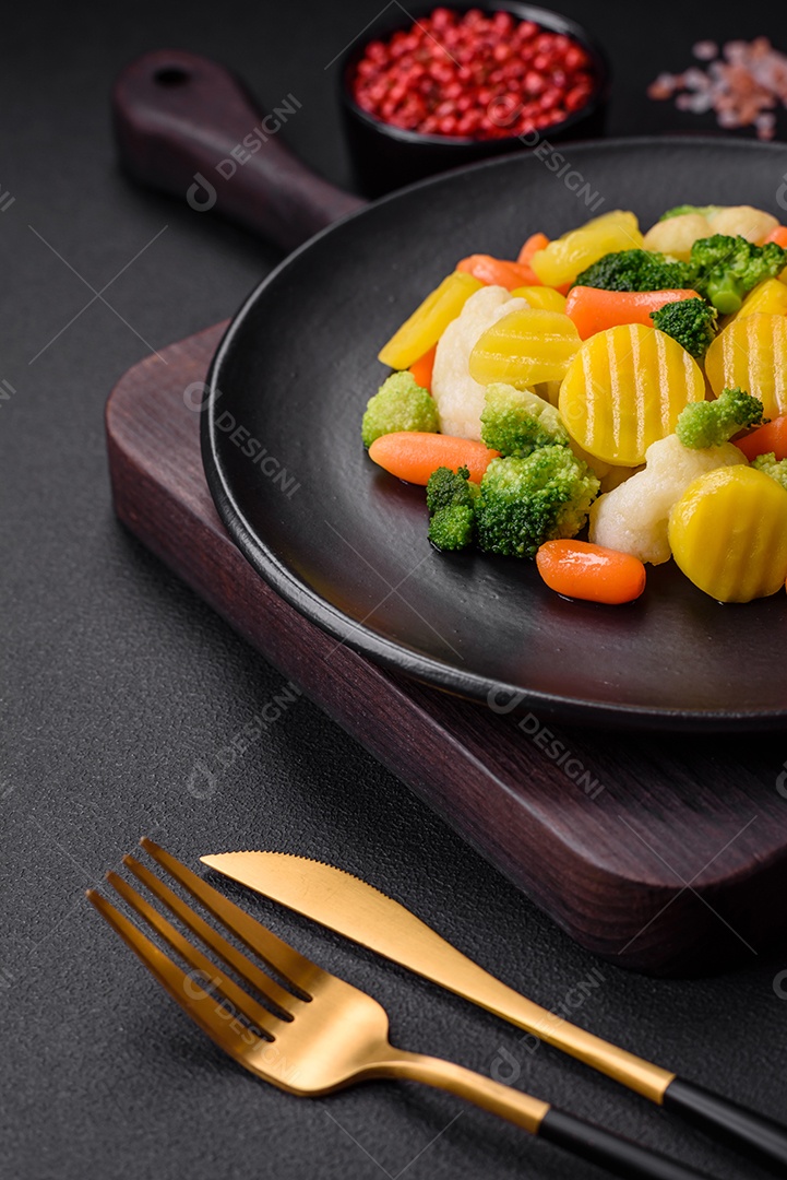 Deliciosos legumes frescos cozidos cenouras, brócolis, couve-flor em uma placa preta sobre um fundo escuro de concreto