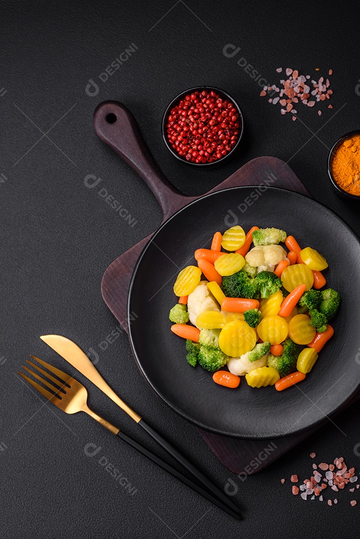 Deliciosos legumes frescos cozidos cenouras, brócolis, couve-flor em uma placa preta sobre um fundo escuro de concreto